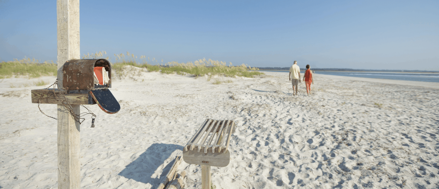 Brievenbus op het strand met post en koppel die in de verte naar de zee loopt