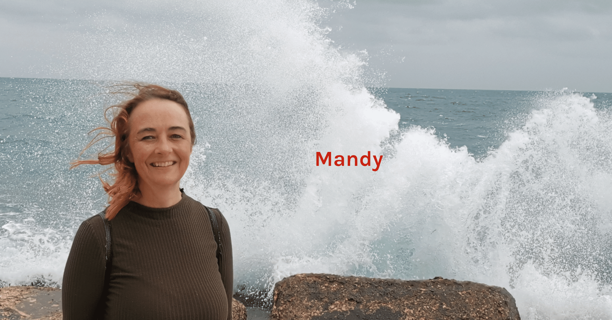 Header Over mij Mandy die losjes en ontspannen staat voor een zee die tegen de kant opklotst