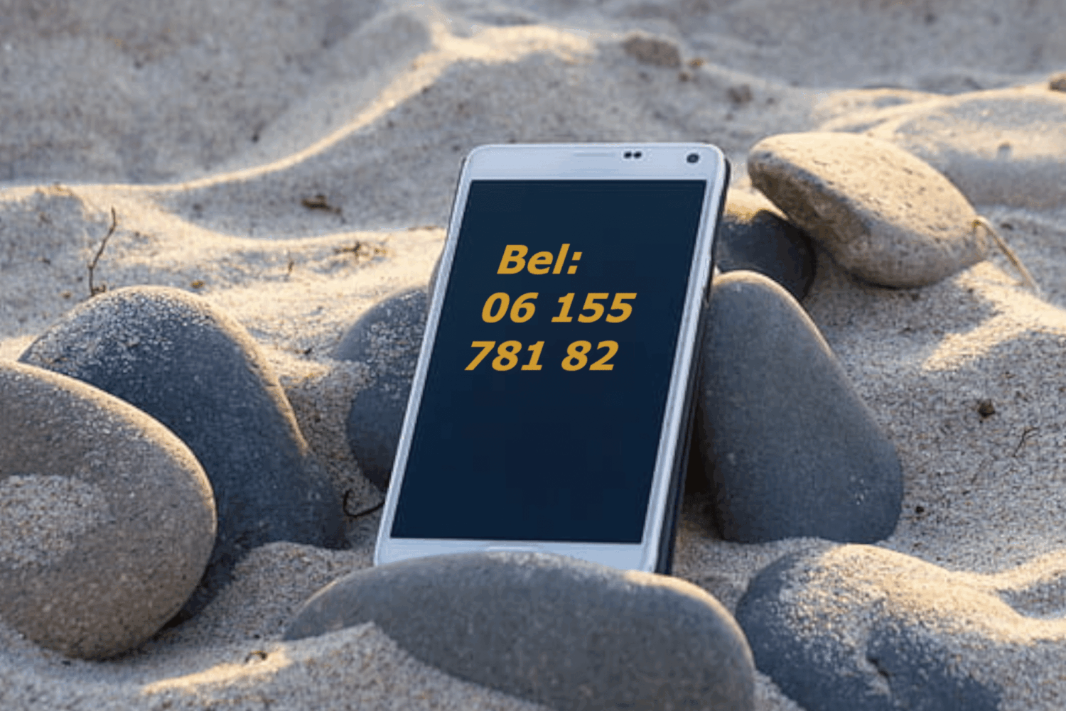 Telefoon tussen stenen in het zand met telefoonnummer Vuurkrachtig 06 155 781 82