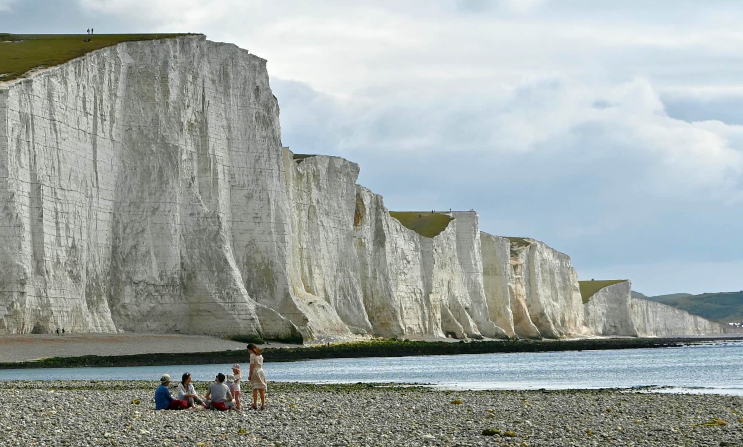Gezin met opa gezellig bijeen op kiezelstrand met witte krijtrotsen